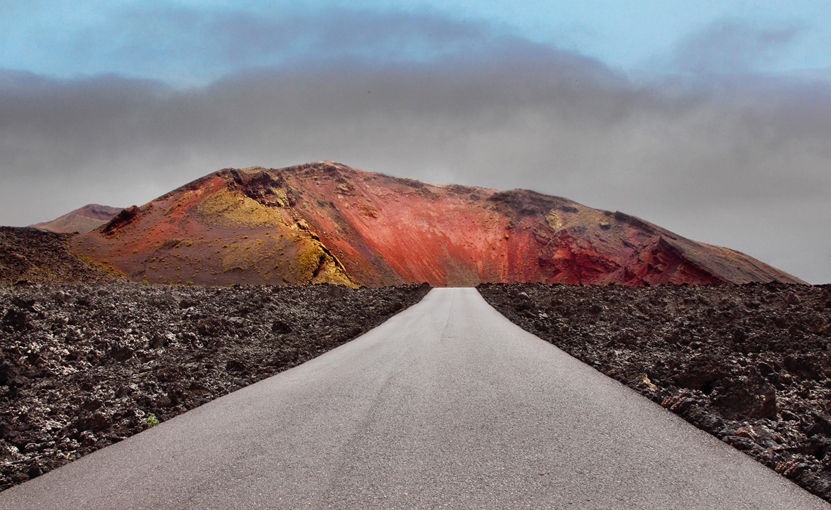 Volcán rojizo en el Parque Nacional de Timanfaya visto desde la carretera, símbolo de la fuerza natural y la necesidad de un diseño respetuoso con el entorno.