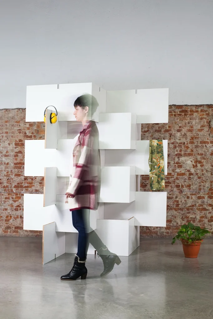 Mujer caminando frente a un biombo de cartón blanco modular BYÓ en un espacio interior con pared de ladrillo visto
