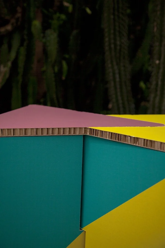 Primer plano del plegado del taburete de cartón INFIX, con cactus difuminados al fondo