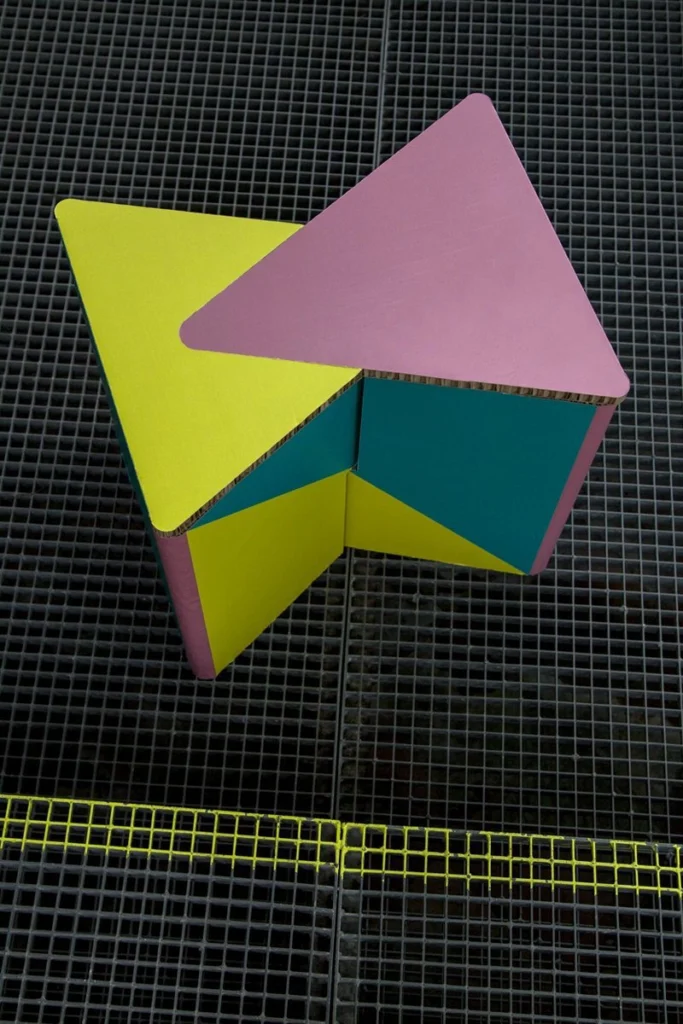 Taburete de cartón impreso INFIX visto desde arriba, con diseño geométrico, sobre fondo de rejilla gris