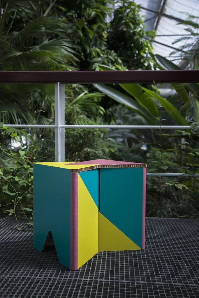 Taburete de cartón impreso INFIX junto a vegetación en un jardín botánico