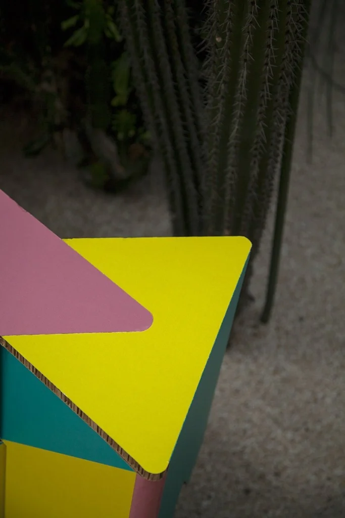 Vista superior en primer plano de una esquina del taburete de cartón INFIX, sobre fondo difuminado con cactus