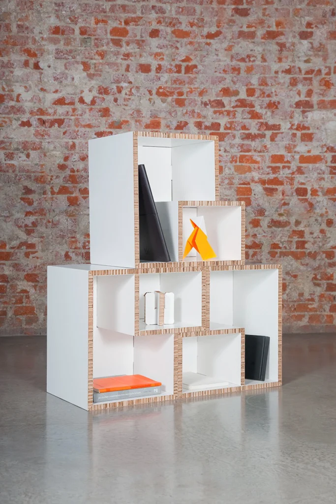 Mueble de cartón modular en composición vertical, sobre fondo de ladrillo y suelo gris